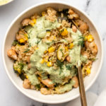 lemon dill quinoa casserole in white bowl topped with green goddess tahini dressing and a gold fork
