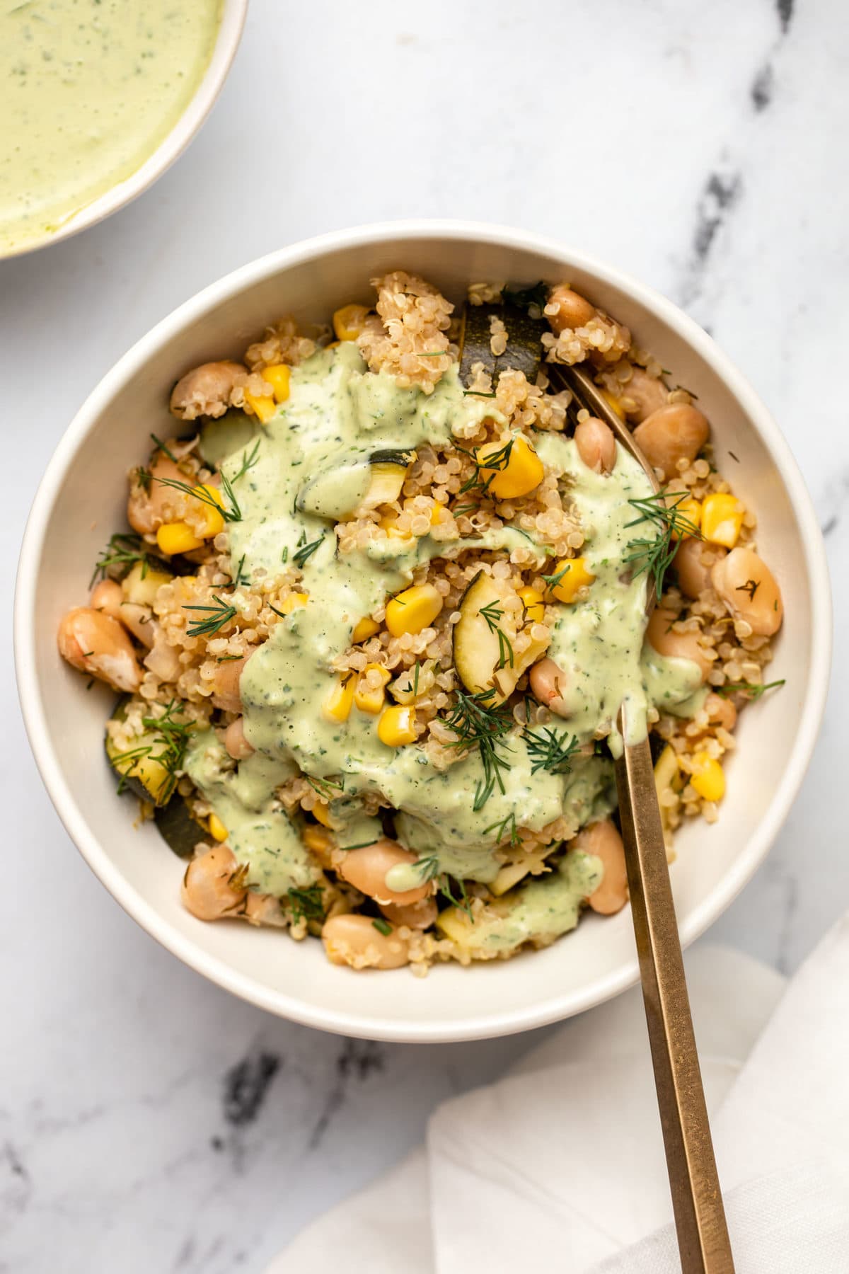 lemon dill quinoa casserole in white bowl topped with green goddess tahini dressing and a gold fork