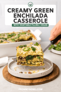 Hand serving slice of vegan creamy green enchilada casserole onto white plate