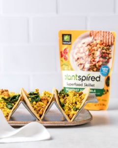 3 tofu breakfast tacos with spinach resting in a taco holder. A bag of Nasoya's Plantspired Breakfast Scramble is in the background off to the right