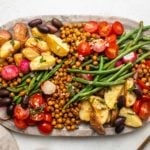 Large stone serving tray of vegan niçoise salad, with dressing on the side and gold serveware