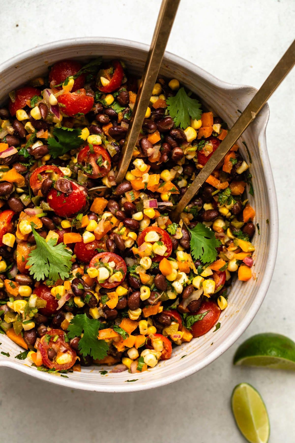 Overhead photo of Tex-Mex black bean salad in large bowl topped with fresh cilantro and gold serving spoons