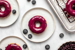 Baked Blueberry Donuts on small white plates with fresh blueberries on marble background
