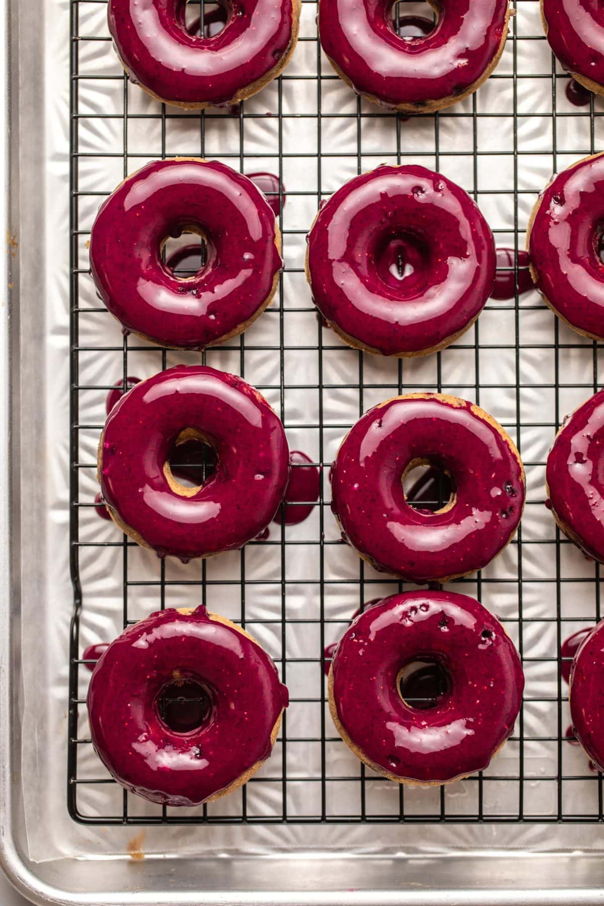 Baked blueberry donuts dunked in blueberry glaze resting on a black cooling rack
