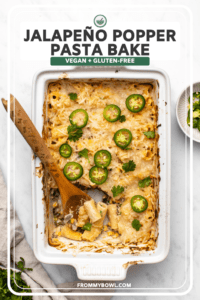 Jalapeño Popper Pasta Bake in white casserole dish after baking, with wooden spoon in the dish and scooping out pasta