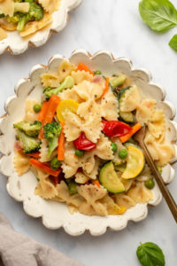 scalloped white plate with pasta primavera - bow ties and mixed colorful vegetables in a light cream sauce