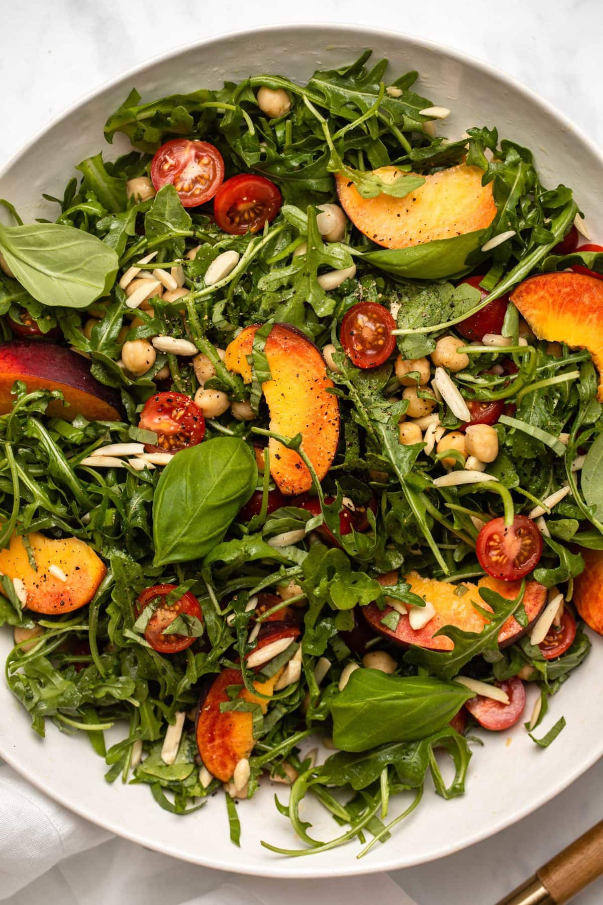 Overhead close-up photo of peach and chickpea salad with arugula, basil, and slivered almonds