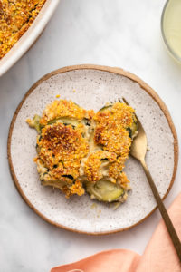 Close-up photo of zucchini gratin on small white plate with gold fork