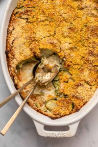 Close-up photo of zucchini gratin in white casserole dish with a scoop taken out of it