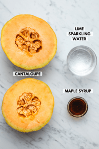Ingredients for cantaloupe slushie on marble background; clockwise text labels read lime sparkling water, maple syrup, and cantaloupe