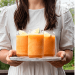 Girl in white dress holding marble tray of 3 cantaloupe slushies with a lime wedge
