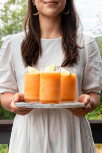 Girl in white dress holding marble tray of 3 cantaloupe slushies with a lime wedge