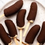 Seven chocolate covered banana pops arranged on a white speckled plate