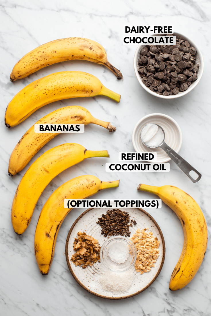 Ingredients for Chocolate Covered Banana Pops on marble background. Clockwise text labels read dairy-free chocolate, refined coconut oil, bananas, and optional toppings