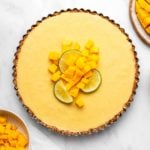 Coconut mango tart topped with lime slices and mango pieces on marble background