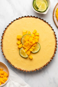Frozen coconut mango tart topped with diced mango and a slice of lime on marble background