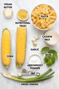 Ingredients for Charred Corn Pasta arranged on marble background. Clockwise text labels read pasta, cashew milk, garlic, basil, salt & pepper, green onions, corn, and vegan butter