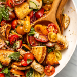 Everything bagel panzanella salad with colorful tomatoes in large white bowl with wooden spoons