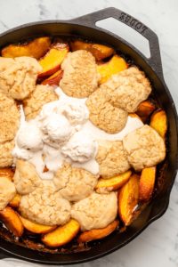 Grilled peach cobbler in cast iron skillet, topped with scoops of melting vanilla ice cream