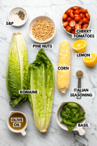 Ingredients for grilled romaine salad on marble background. Clockwise text labels read cherry tomatoes, lemon, corn, italian seasoning, basil, olive oil, romaine, salt, pepper, and pine nuts