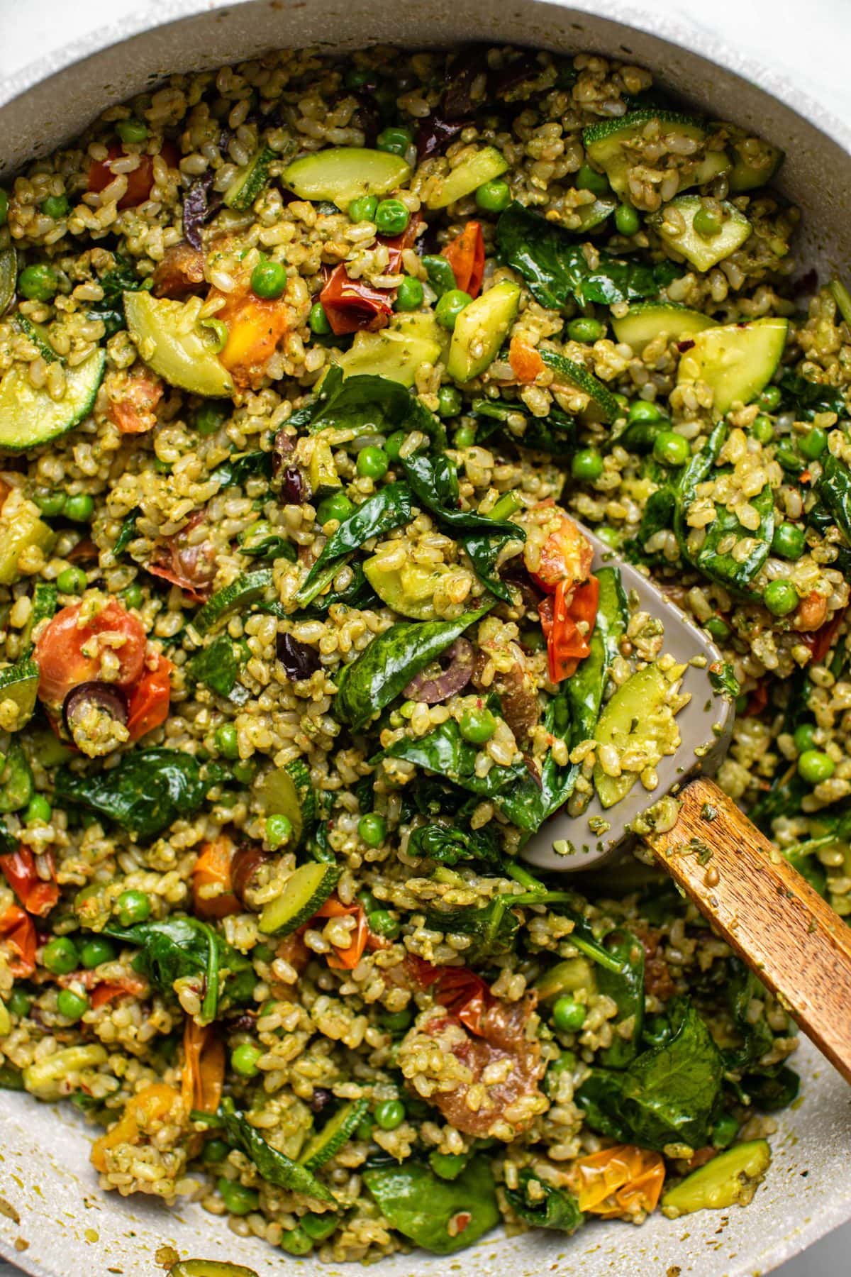 Close up photo of cooked pesto fried rice in large sauté pan with a gray spatula.