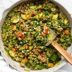 Pesto Fried Rice with Tomatoes, olives, spinach and pine nuts in large sauté pan on marble background