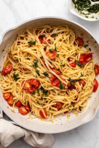 Roasted cherry tomato pasta topped with basil gremolata in a large sauté pan. A bowl of basil gremolata sits off to the side