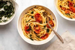 Roasted tomato pasta with basil gremolata in white bowl with silver fork on marble background