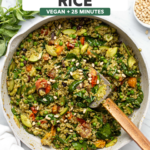 Pesto Fried Rice with Tomatoes, olives, spinach and pine nuts in large sauté pan on marble background