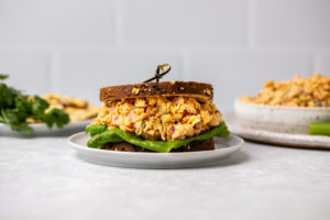 Buffalo chickpea salad in a sandwich with lettuce on a small plate, on a marble background
