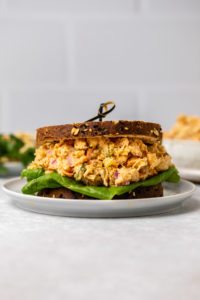 Buffalo chickpea salad in a sandwich with toasted grain bread and a piece of butter lettuce.