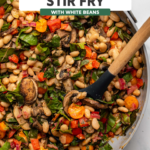 White bean stir fry with vegetables in large sauté pan with wooden spoon