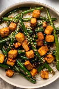 close-up overhead photo of green beans and crispy tofu over white rice