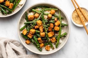 Garlic Green Bean Stir Fry with Crispy Tofu over white rice in large bowl on marble background