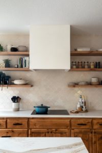 Cozy warm kitchen show with a white vent hood, tile backsplash, and open shelving