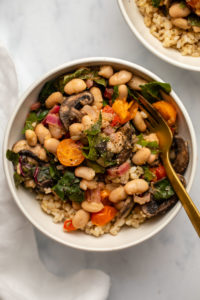 Summer white bean stir fry in white bowl with gold fork
