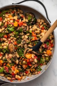 White bean stir fry with vegetables in large sauté pan with wooden spoon