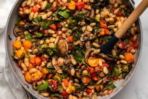 Large sauté pan of white bean skillet with colorful sauteed summer vegetables