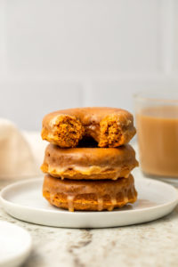 Stack of pumpkin chai spiced donuts topped with glaze on white plate with chai in the background