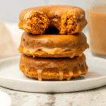 Stack of pumpkin chai spiced donuts topped with glaze on white plate with chai in the background