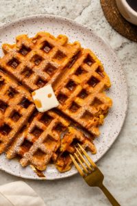 Close-up photo of waffle topped with vegan butter and a drizzle of maple syrup