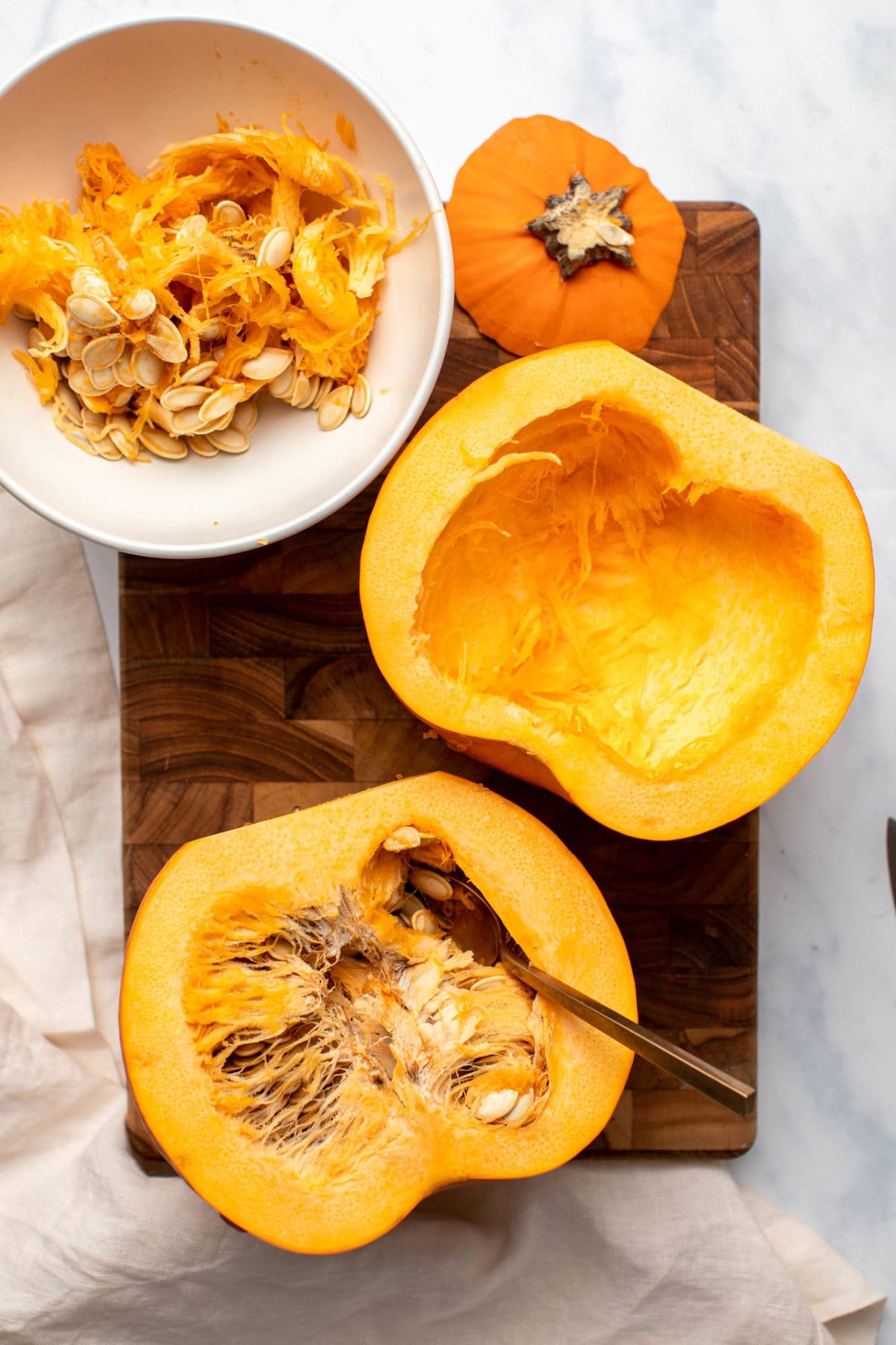 Pie pumpkin cut in half, with one half de-seeded and the other half being scooped out with a spoon