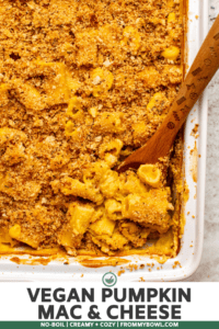 Close-up photo of baked pumpkin mac & cheese in white casserole dish with a wooden spoons scooping the pasta