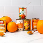 Cans of pumpkin puree arranged with pie pumpkins on marble kitchen countertop