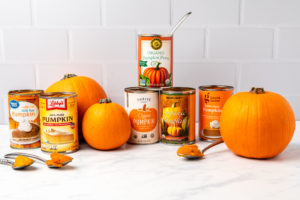 Cans of pumpkin puree arranged with pie pumpkins on marble kitchen countertop