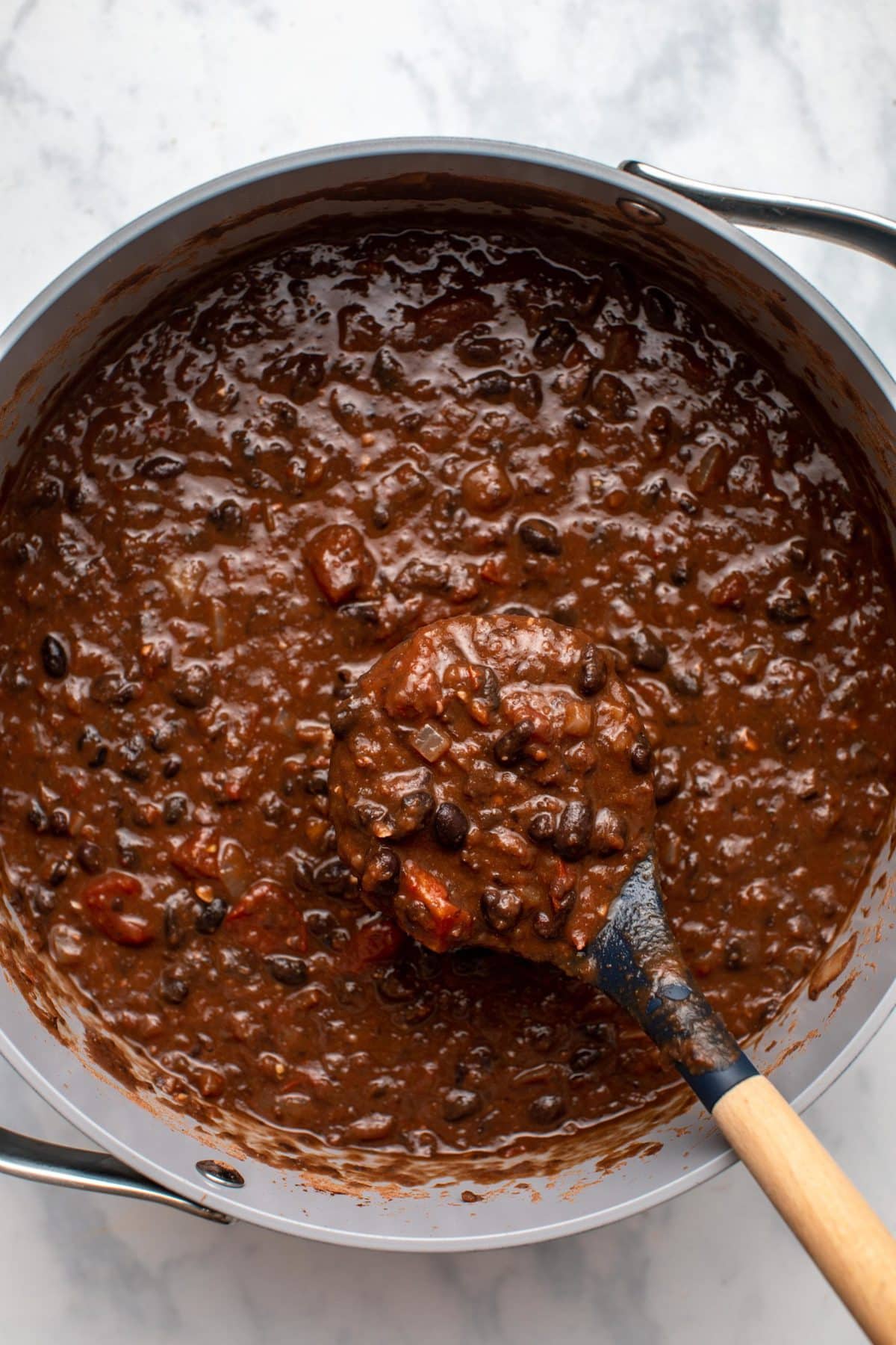 Large pot of black bean chili with wooden scoop scooping chili to show texture