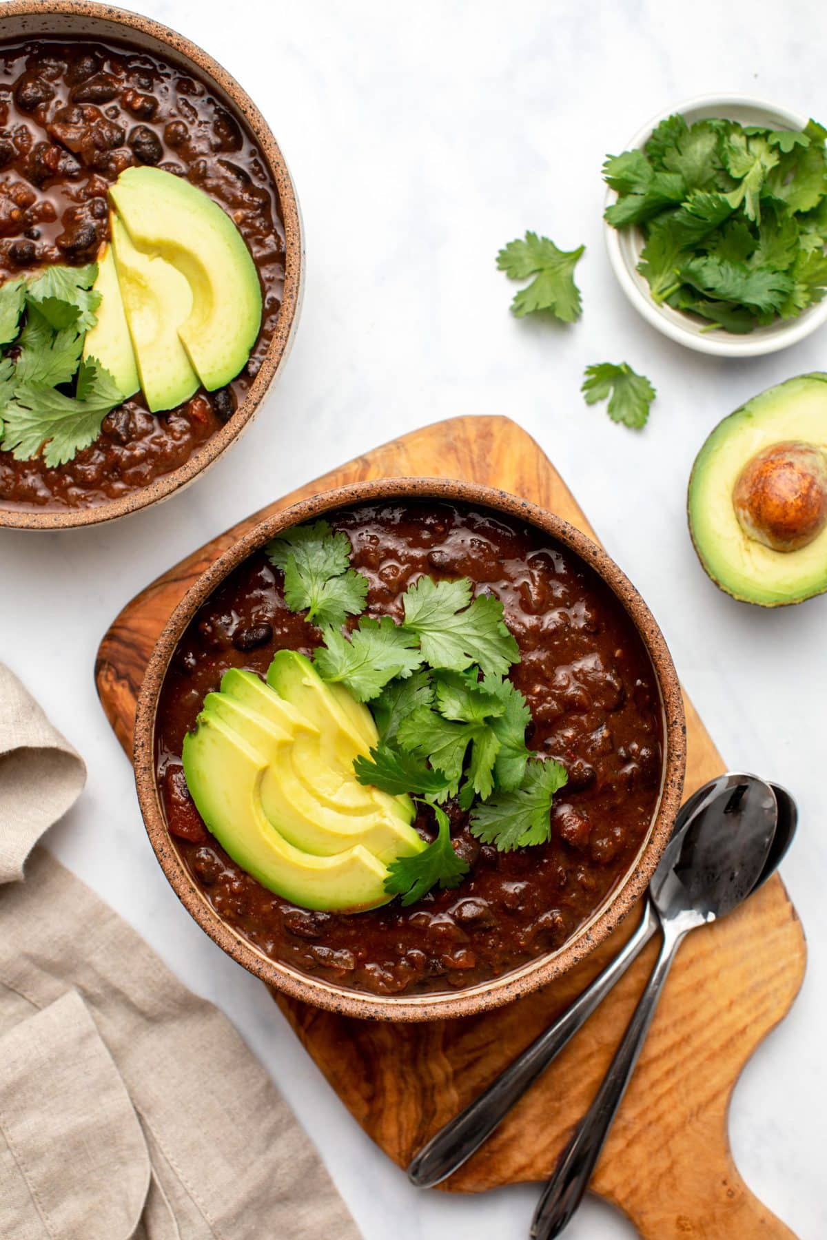 Two bowls of black bean chili topped with avocado and cilantro with sliced avocados on the side