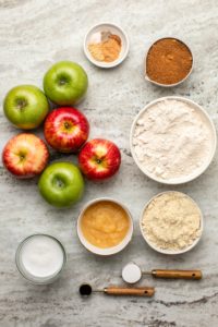 Ingredients for vegan apple cake in small white bowls on stone background