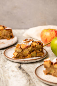 slice of apple cake on plate surrounded by fresh apples