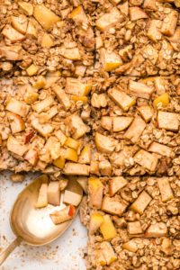 Close-up photo of sliced apple cinnamon oatmeal in baking dish with a golden spoon